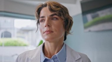 Modern klinikte ciddi bir pratisyen bekleme randevusu var. Hastane ofisinde beyaz üniformayla duran orta yaşlı kadın doktor. Portre uzmanı tıbbi bakım sağlamaya hazır.