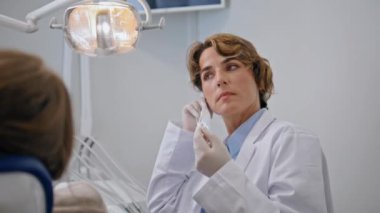 Stomatoloji uzmanı koruyucu maske takmaya hazırlanıyor. Kadın doktor diş hekimliği kliniğinde ağız muayenesine başlıyor. Hastanedeki hasta dişçi muayenesini bekliyor.