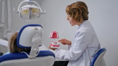 Modern klinikte çocuk hastalarına ağız hijyeni öğreten bir doktor. Kadın dişçi muayenede diş bakımını anlatıyor. Stomatolog küçük çocuğu dişçide eğitiyor.. 