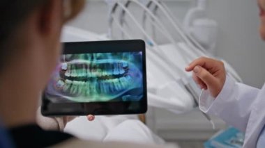 Klinik ziyaretindeki hastaya dijital röntgen sonuçlarını gösteren dişçi. Bilinmeyen kadın stomatolog diş hekimliğinde detaylı bir ağız sağlığı açıklaması yapıyor. Doktor diş tedavisi seçeneklerini tartışıyor.