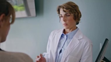 Terapist, muayene merkezindeki kadın hastaya tedavi planını açıklıyor. Hastane ziyaretçisi doktor teşhisini dikkatle dinliyor. Kadın doktor randevuda konuşuyor..