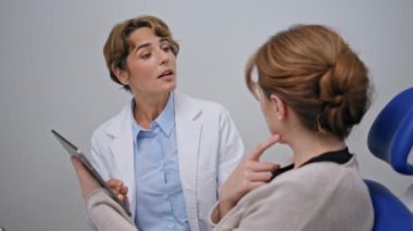 Doktor, klinikteki stomatoloji konsültasyonundaki hastaya ait diş röntgeni sonuçlarını analiz ediyor. Profesyonel, dişçilikte dijital diş görüntülerini tartışıyor. Orta yaşlı bir kadın ağız boşluğu röntgenini inceliyor..