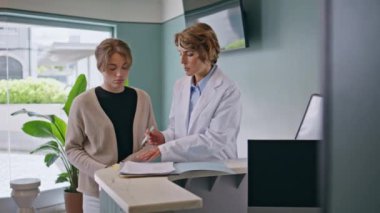 Kadın doktor, sağlık kliniğindeki kadın hastaya sigorta detaylarını anlatıyor. Kız ziyaretçi, sağlık hizmetleri bürosunda profesyonel danışmanlık yaptıktan sonra tedavi planını imzalıyor. Doktor randevusu.