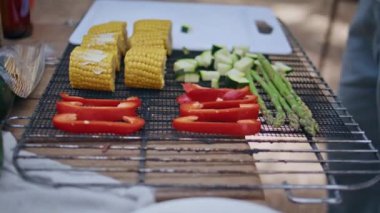 Izgarada taze sebzeler yaz barbeküsü için hazır. Bilinmeyen kişi güneşli ormanda mısır çanı biberi ve kabak pişiriyor. Sağlıklı malzemeler, doğada besleyici yemekler için düzenli olarak düzenlenir.