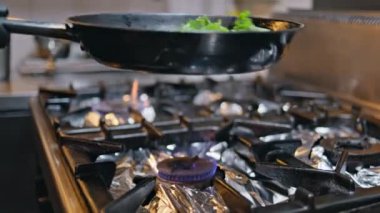 Aşçı tavada yeşil sebze pişiriyor, modern mutfağın üzerinde. Lokanta fırınında taze marul kızartan kimliği belirsiz bir adam. Elleri siyah eldivenli, kafeteryadaki malzemeli kızartma makinesini tutuyor.