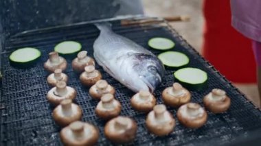Doğa pikniğinde kömürde kızartılan yakın yemek. Orman barbeküsünde taze mantar, balık kabağı. Kimliği belirsiz bir kadın dışarıda kömürde sağlıklı yemek pişiriyor. Gençlerin bbq toplantısı var..