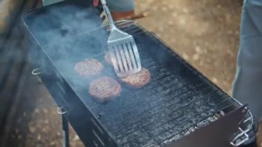 Sunny Forest 'ta barbeküde cheeseburger pişiren adam. Dışarıdaki kömürlere hazırlanan köftelere peynir dilimleri ekleyen bilinmeyen bir adam. Genç tatilci parkta barbekü partisinin tadını çıkarın..