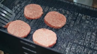 Orman pikniğinde ızgarada pişmiş çiğ hamburger köfteleri. Bilinmeyen kişi açık hava yemeği için barbeküde taze et pişiriyor. Adam hafta sonu barbeküsünde hamburgerler için kömür üzerine lezzetli et hazırlıyor..