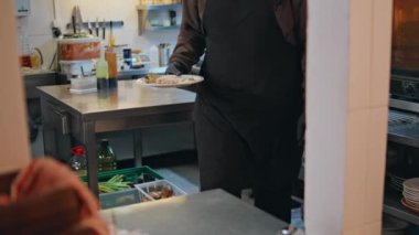 Şef servis tabağını profesyonel mutfak fotoğrafına koyuyor. Bilinmeyen garson müşteriye soslu fırında sebze tabağı götürüyor. Restoran çalışanları mükemmel yemek servisi için işbirliği yapıyorlar..