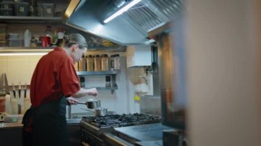 Pan modern restoranda sosu hazırlayan mutfak çalışanı. Genç kadın aşçı kaşık ile mutfak ocağında lezzetli yemekler pişiriyor. Ciddi kadın aşçı karıştırıcı yemek pişiriyor. Yemek pişirme yerinde sos yapıyor..