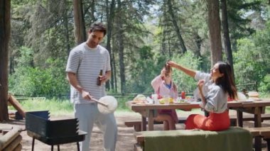 Grup arkadaşları güzel parkta barbekü pikniğinin tadını çıkarıyorlar. Adam yemek pişiriyor, masada iki kadınla bira içiyor. Neşeli insanlarla buluşup yeşil güneşli ormanda bbq hazırlıyorlar. Arkadaşlık kavramı