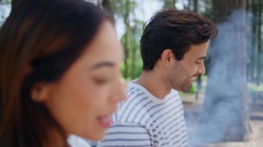 Parkta arkadaşça sohbet eden gülümseyen bir çift. Etrafı doğa tarafından çevrili. Mutlu genç insanlar bilinmeyen arkadaşlarıyla iletişim kurarak kaygısız bbq pikniğinin tadını çıkarıyorlar. Ormanda gülen çift konuşuyor.