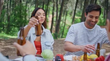Kadınlar ve erkekler orman pikniğinde yemek içmekten zevk alıyorlar. Mutlu arkadaşlar Green Park 'ta rahat bir hafta sonu toplantısında bira şişelerini kızartıyorlar. Gülümseyen grup yeşilliklerle çevrili tasasız bir günü paylaşıyor..