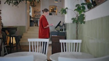 Restoranda masa temizleyen kadın, kırmızı üniforma giyiyor. Bayan personel yemek salonunu düzenliyor, misafirler için kafe hazırlıyor. Küçük, rahat bir kafeteryada çalışan garson kız. Profesyonel hizmet..