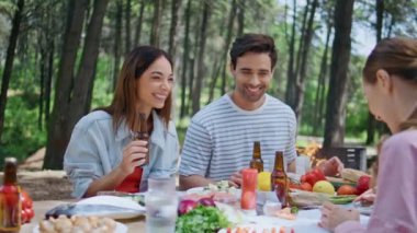 Arkadaşlar orman pikniğinde gülüyor, BBC partisinde birlikte eğleniyorlar. Bira içen mutlu insanlar, Yeşil Park 'ta rahat bir hafta sonunun tadını çıkarıyorlar. Gülümseyen grup yeşilliklerle çevrili ormanda sosyalleşiyor..