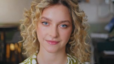 Çekici sarışın kadın portresi. Nazikçe gülümseyen bir kamera. Küçük bir restoranda tek başına oturan genç ve güzel bir bayan. Zarif bluzuyla kafeteryada poz veren pozitif kıvırcık kız