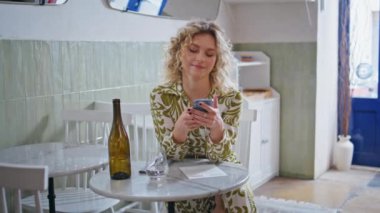Tasasız kadın elinde akıllı telefonuyla modern kahvede tek başına oturuyor. Samimi bir restoranda cep telefonu mesajı okuyan gülümseyen kıvırcık kadın. Kafedeki iş molasında rahat görünen iş kadını.