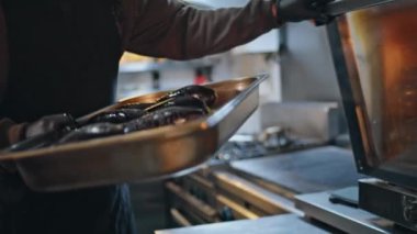 Şef patlıcanları yakın çekim için fırına koyuyor. Lokanta mutfağında çalışan tanınmamış bir profesyonel taze sebzeleri sağlıklı yemek için hazırlıyor. Adam mutfak çalışma alanındaki aşçılık sürecine odaklanmış.