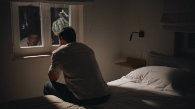 Depresyonda olan adam gece pencerenin kenarında oturmuş endişeli hissediyor. Karanlık yatak odasındaki sorunları düşünen düşünceli bir adamın yansıması. Siluet adam yatakta yalnızlık ve gerilim yaşıyor..