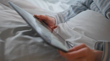 Kızın elleri tableti sabah yatağında tutuyor. Çizgili pijamalı kimliği belirsiz bir kadın öğrenci yatak odasındaki bilgisayardan eğitim semineri izliyor. İş kadını yalan söyleyen yastıkları okuyor.