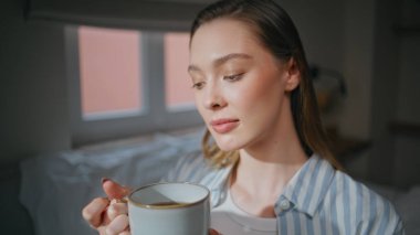 Dairenin yatak odasında sabah kahvesi içen bir kadın. Huzurlu bir kadın portresi çizgili pijama giymiş, elinde sıcak bir kupayla huzurlu bir zevk gösteriyordu. Rahat bir ortamda içkisini yudumlayan sakin bir kız. 