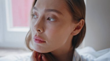Yatak odasında poz veren güzel bir model doğal güzelliği yakından gösteriyor. Düşünceli kadın, düşünceli ve sakin ifadesiyle beyaz odada kameraya bakıyor. Sabah vakti ciddi bir kızın portresi.