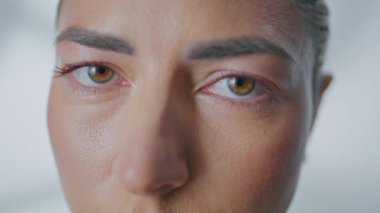 Güneşin altında kameraya bakan sakin kadın gözleri. Beyaz duvar zeminine dik dik bakan güzel bir kız portresi. Sabah ışığı doğal güzelliğin altını çizer. Sakin ifade iç huzuru yansıtır