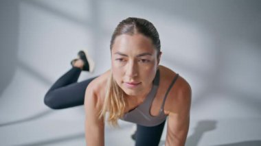 Aktif sporcu kadın, yakın çekimde bacağını kaldırıyor. Sportif kadın vücut egzersizi. Yoga minderiyle egzersiz yapan zayıf bir bayan. Atletik kız eğitimi tek başına yerde diz çöküp beyaz stüdyo arka planında esniyor.