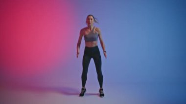 Zinde bir kız neon odada yüksek atlama egzersizi yapıyor. Spor kulübünde kadın sporcu kardiyo çalışması. Fitness kadın zayıflama eğitimi. Profesyonel koşucu vücut kaslarını ısıtır. Sağlıklı yaşam tarzı 