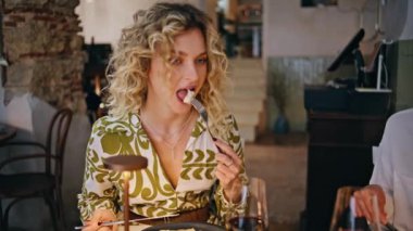 Gülümseyen kadın, arkadaşlarıyla yemek yiyor. Akşamı modern restoranda yakın planda geçiriyor. Kıvırcık sarışın gurme yemeğinin tadını çıkarıyor ve iş arkadaşlarıyla eğleniyor. Kafeteryadaki arkadaş canlısı şirkette şık bir bayan yemek yiyor..