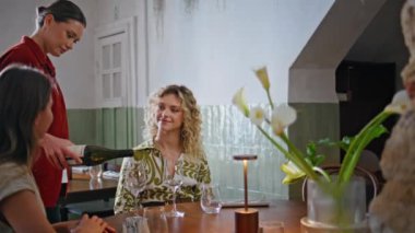 Kızlar restoranda dostça buluşmanın tadını çıkarırlar. Kadın garson restoran masasında bardaklara şarap dolduruyor. İki bayan, kafeteryada rahat bir şekilde toplanmanın keyfini çıkarıyorlar. Arkadaş iletişimi