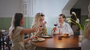 Kadın meslektaşlar kafeteryada oturmuş şarap kadehlerini kızartıyorlar. Birlikte yemek yiyen üç bayan şık bir restoranda şenlikli, dostane bir ortam yaratıyor. Grup kızları rahat bir kafede kutlama yapıyorlar..