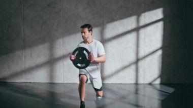 Spor kulübünde ağırlık plakası tutan güçlü adam hamleler yapıyor. Ağırlık kaldırma egzersizi sırasında ağır ekipman kullanan ciddi bir adam. Esmer kaldırıcı bisepsi pompalıyor. Çatı katında sporcu eğitimi