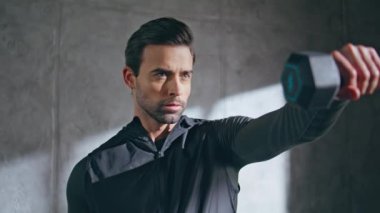 Çatıkatındaki stüdyoda dambıl egzersizi yapan odaklanmış bir sporcu. Gergin güçlü adam spor malzemelerini kaldırıyor güçlü eller kaslarını içeride çalıştırıyor. Kas formundaki vücut için sağlıklı sporcu çalışması 