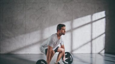 Güçlü adam spor salonunda halter tutarak egzersiz yapıyor. Bacak kaslarını çalıştıran sportif bir adam. Güç toplayıcı erkek, antrenmandan önce ağır nefes alıyor. Spor yaparken kaslı sporcu ağırlık kaldırıyor. 