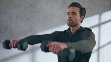 Dambılları kaldıran odaklanmış bir adam spor salonunun kapısında egzersiz yapıyor. Fitness sporcusu, sırayla ağırlık egzersizi yapıyor. Güçlü motivasyonlu esmer kasları evde tek başına çalıştırıyor. Spor konsepti