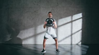 Spor eğitmeni hafif stüdyoda ağırlık plakası kullanarak hamleler yapıyor. İyi tanımlanmış kasları olan güçlü bir adam spor salonunda güç ve teknik gösterisi yapıyor. Egzersiz yapan motive bir adam.