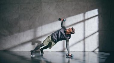 Güçlü sporcu güçlü eller kaslarını tahta pozisyonunda çalıştırıyor. Gri tavan arası stüdyosunda her gün ışık alan kaslı vücut çalışması yapan sağlıklı bir adam. Esmer sporcu spor salonunda tek başına kaldırıyor. Spor konsepti