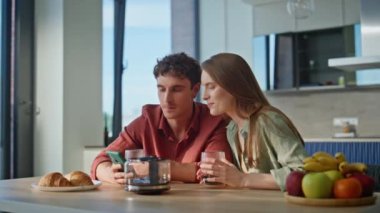 Rahat çift, ev mutfağında birlikte akıllı telefonu paylaşıyor. Sevgili eşler kahvaltıda yan yana oturup cep telefonundan haberleri tartışıyorlar. Gülümseyen mutlu çift sabah iletişim kuruyor.