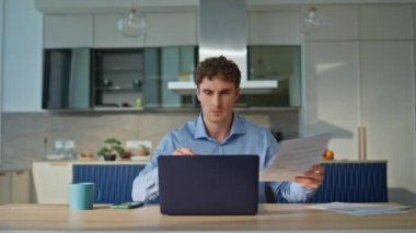 Modern ofis bilgisayarında çalışan ciddi bir adam, belgeleri inceliyor. Evrak işleri ve dijital görevler arasında birden fazla işi olan profesyonel bir serbest çalışan. Uzaktan kumandalı bir işe odaklanmış bir iş adamı..