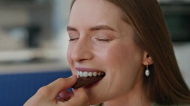 Mutlu kadın çikolata kapaklı gözleri ısırıyor tatmin olmuş yüz ifadesiyle yakından. Sevgi dolu bir adam kız arkadaşını lezzetli şekerlerle besliyor. Neşeli kız evde erkek arkadaşıyla tatlı yiyor..