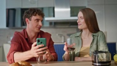 Neşeli eşler sabah evde kahvelerini yudumlarken erkek eli cep telefonlarına bakarlar. Mutfak masasında birlikte içki içen gülümseyen çift. Mutlu çift konuşmaları telefon paylaşımı gündelik anlarında
