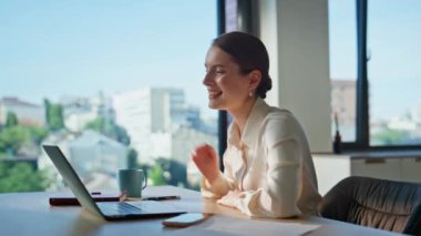 Girişimci çevrimiçi konferansta konuşuyor. Yakın ofisteki laptop web kamerasına işaret ediyor. Gülümseyen kadın, kurumsal işyerindeki işi tartışırken sanal bir toplantı yapıyor. Serbest çalışan kadın video çağrısı