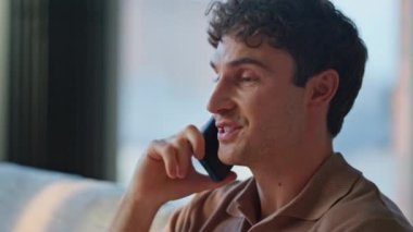 Evdeki adam cep telefonuyla konuşuyor rahat bir kanepede dinleniyor. Akıllı telefon görüşmesiyle haberleri tartışan olumlu adam rahat koltukta oturuyor. Gülümseyen erkek içeride arkadaşça telefon görüşmesi yapar..