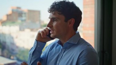 Endişeli yönetici ofisteki panoramik pencerenin önünde cep telefonuyla tartışıyor. Sinirli iş adamı, akıllı telefon konuşmasında problemden şikayetçi. Kızgın duygusal adam iş yerinde başarısızlığı tartışıyor.