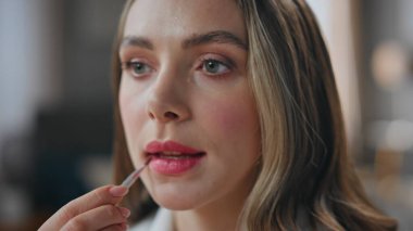 Evde dudaklarını boyayan yakın plan kadın. Tımarhane modeli pembe renkli merhem sürerek evin içinde eğleniyor. Yüz makyajı yapan rahat bir kadın hafif dairede gül nemlendirici ruj sürüyor. 