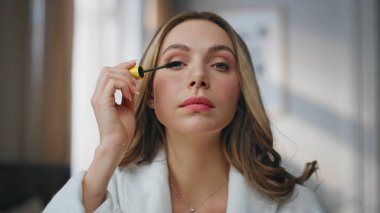 Kirpiklerine rimel süren zavallı bir kadın. Gülümseyen model kamera romantik bir makyaj yapıyor. Çekici bayan evde yapılacak partiye hazırlanan yansımaya hayran. Görünüm kadınlığı kavramı