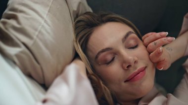 Sabahın erken saatlerinde rahat bir yatakta uyanan gülümseyen bayan. Mutlu çekici kız, güzel bir rüyadan sonra yatak odasında yumuşak güneş ışığının tadını çıkarır. Tasasız genç kadın hafta sonu kendini rahat hissederek evde uzanıyor. 