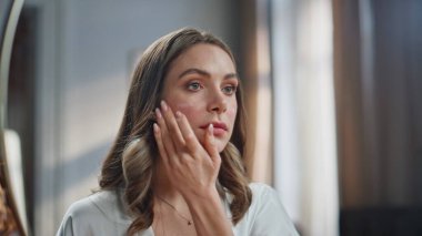 Portre kadını içeride yüz kremini nemlendiriyor. Rahatlamış bir kadın sabahları cildini nemlendiriyor. Gülümseyen bir model, aynaya bakıp, yakından pohpohluyor. Kadınsı günlük prosedürler 