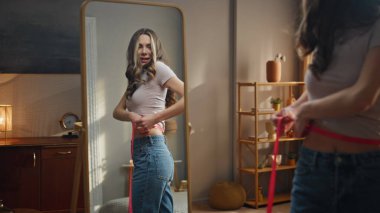 Bel ölçüsünü bantla ölçen kadın yansıması. Mutlu ince model kilo kaybı mükemmel vücut şekline hayran kalıyor. Çekici kız evde fitness başarısını analiz ediyor. Belirleyici başarı konsepti